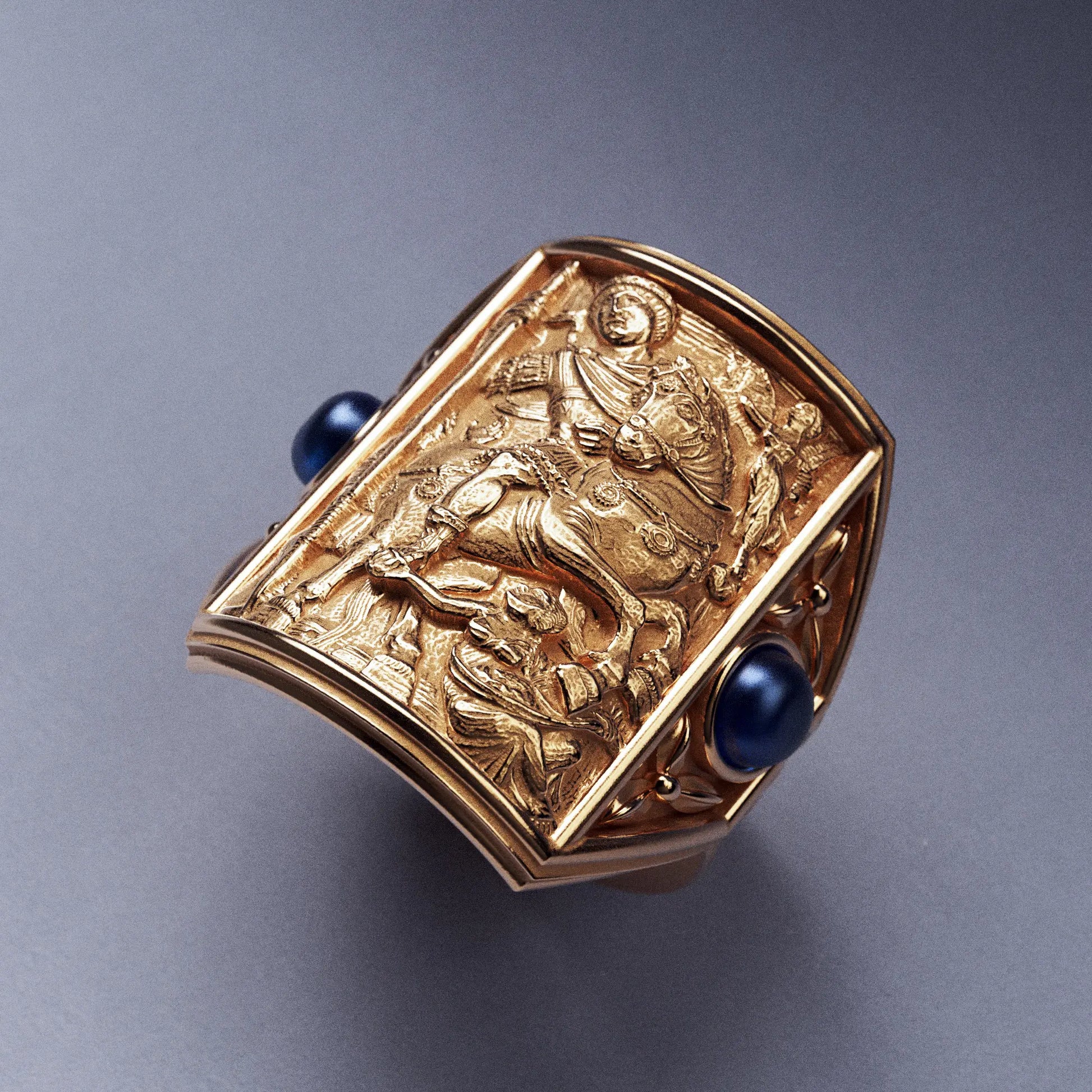 Gold ring with cabochon sapphires and Byzantine-style relief sculpture, featuring intricate details and a regal design.