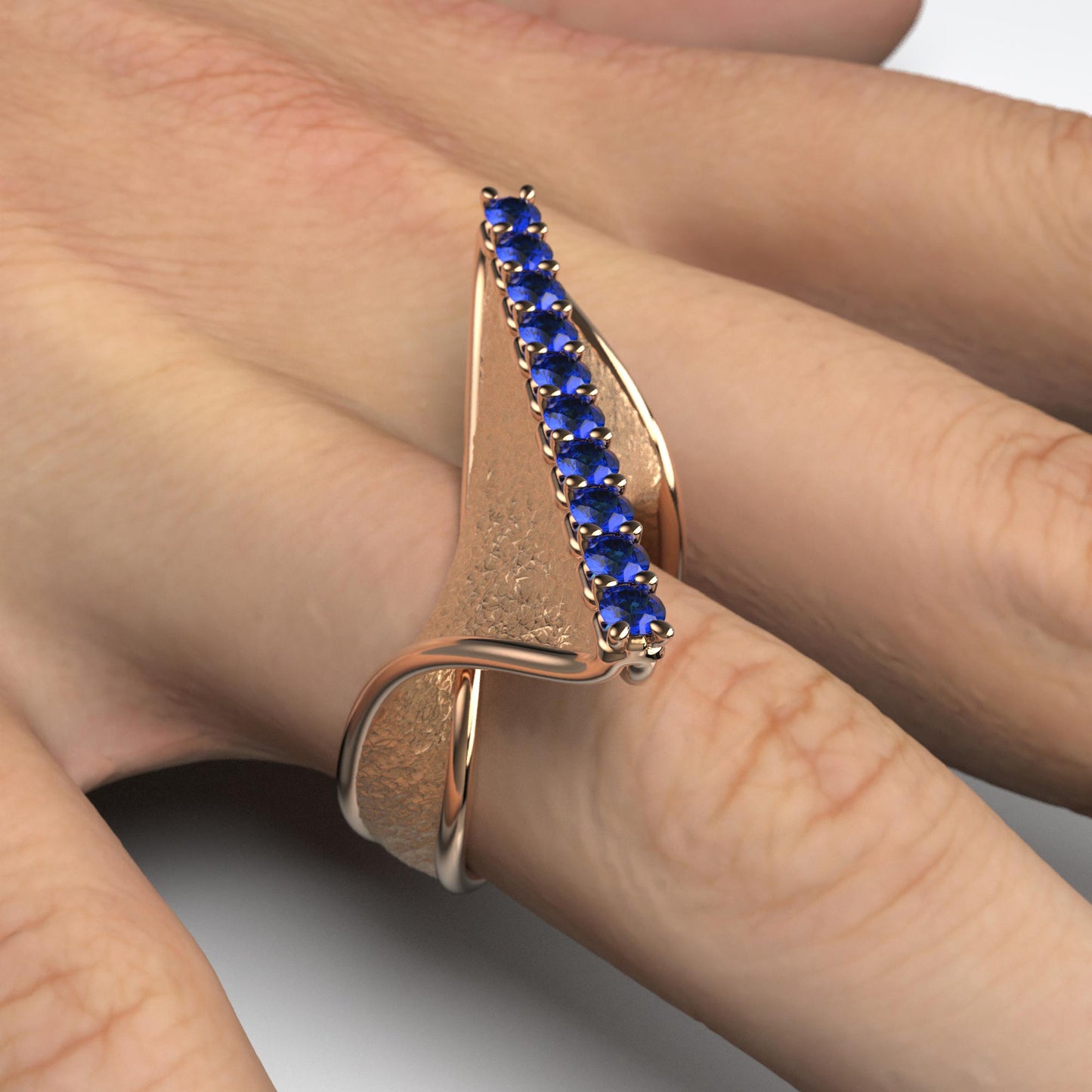 A handcrafted 18k gold ring featuring a modern twisted design with 10 round blue sapphires set along the top ridge. Polished edges with an earth-textured surface.