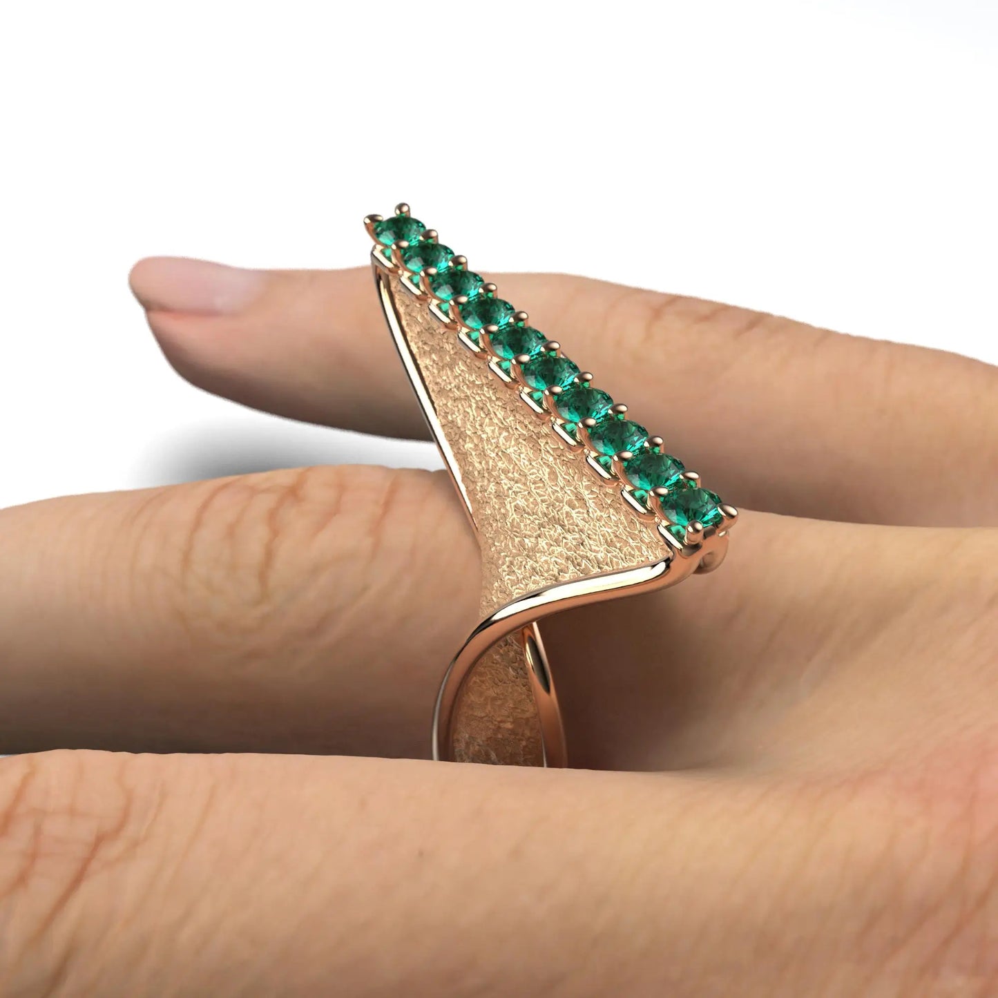 A modern twisted gold ring featuring 10 round natural emeralds set along the top ridge, with polished edges and an earth-textured surface.